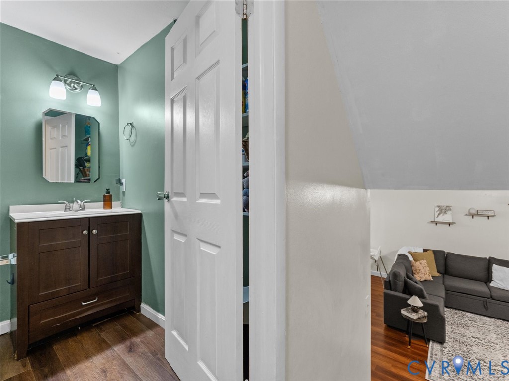 Dark wood vanity with a stone countertop, wall-mounted two-light fixture, bevel-edged mirror, and wood-finish flooring