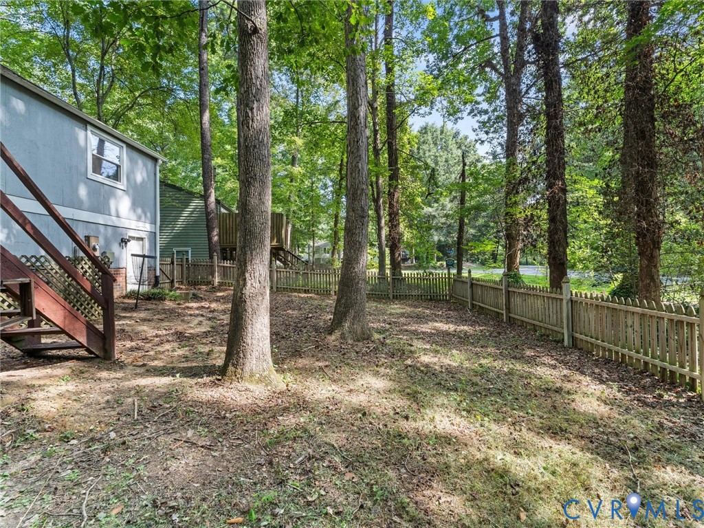 Wooded backyard featuring mature trees, a wooden picket perimeter fence, and an elevated wood staircase