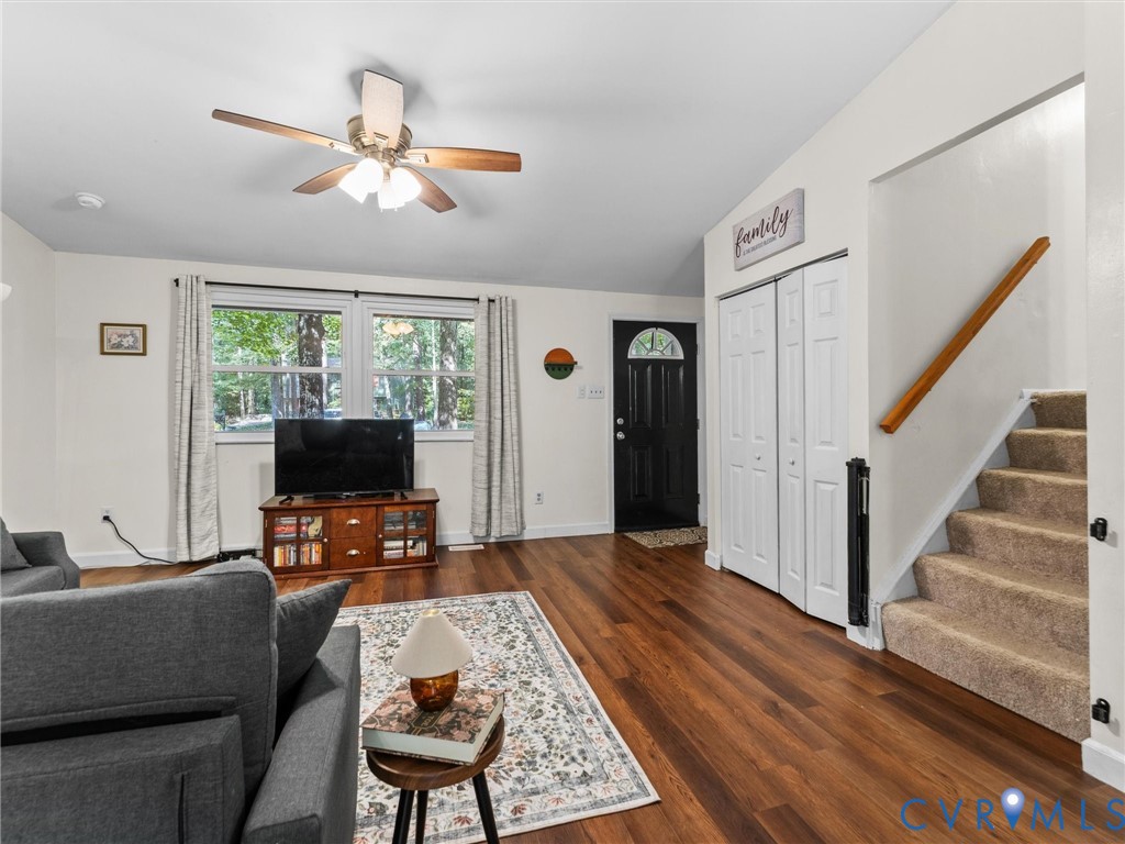 Vaulted ceiling with integrated multi-light ceiling fan, wood-finish flooring, dual-panel closet doors, and staircase with wooden handrail