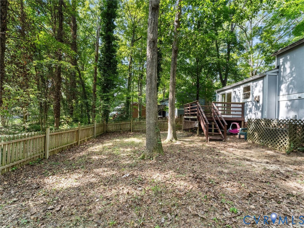 Backyard featuring a wood deck, wood picket fencing, lattice screening, and mature trees
