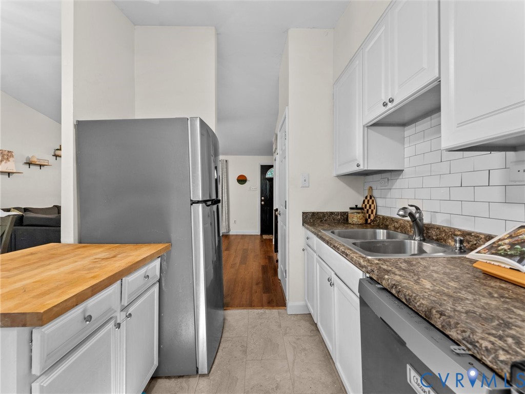 Kitchen featuring white cabinetry, subway tile backsplash, stone-finish countertops, stainless steel appliances, and a wood-finish peninsula countertop