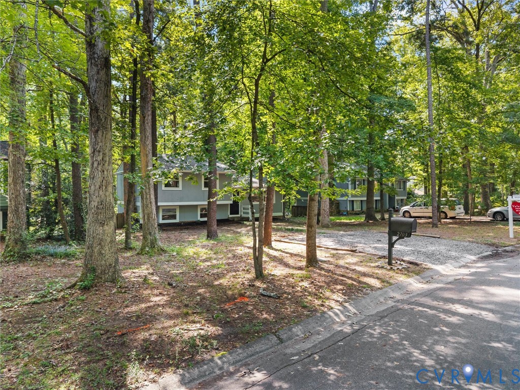 Two-story residence featuring light gray siding, a gravel driveway, and a natural, wooded lot