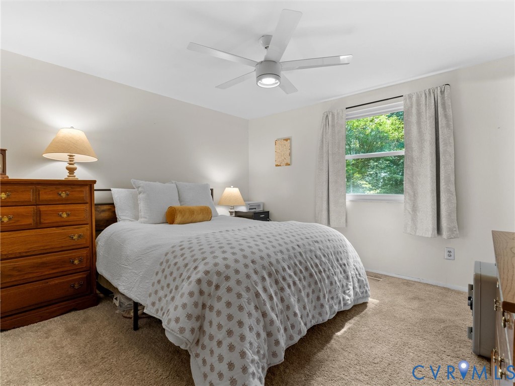 Neutral-toned bedroom featuring plush wall-to-wall carpeting, a multi-blade ceiling fan with integrated lighting, and a single-pane window