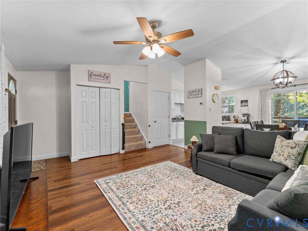 Living area featuring wood-finish flooring, vaulted ceilings with a multi-blade ceiling fan, and sliding glass doors with exterior access