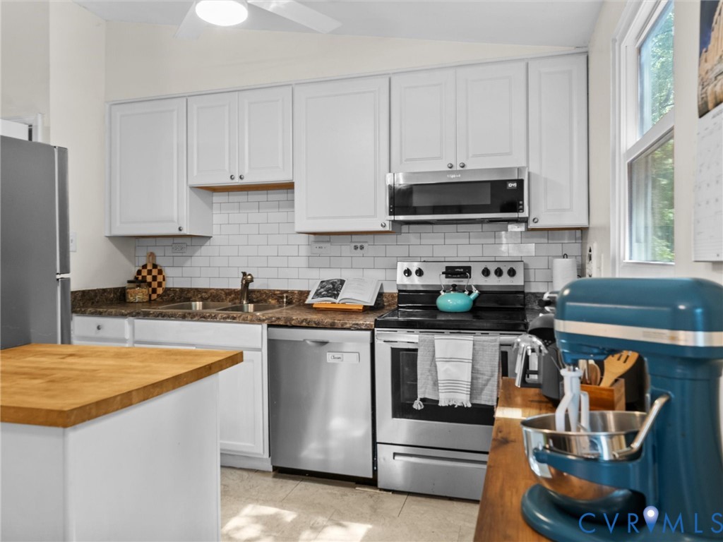 Kitchen featuring white shaker-style cabinetry, a white subway tile backsplash, stainless steel appliances, and a wood-finish countertop