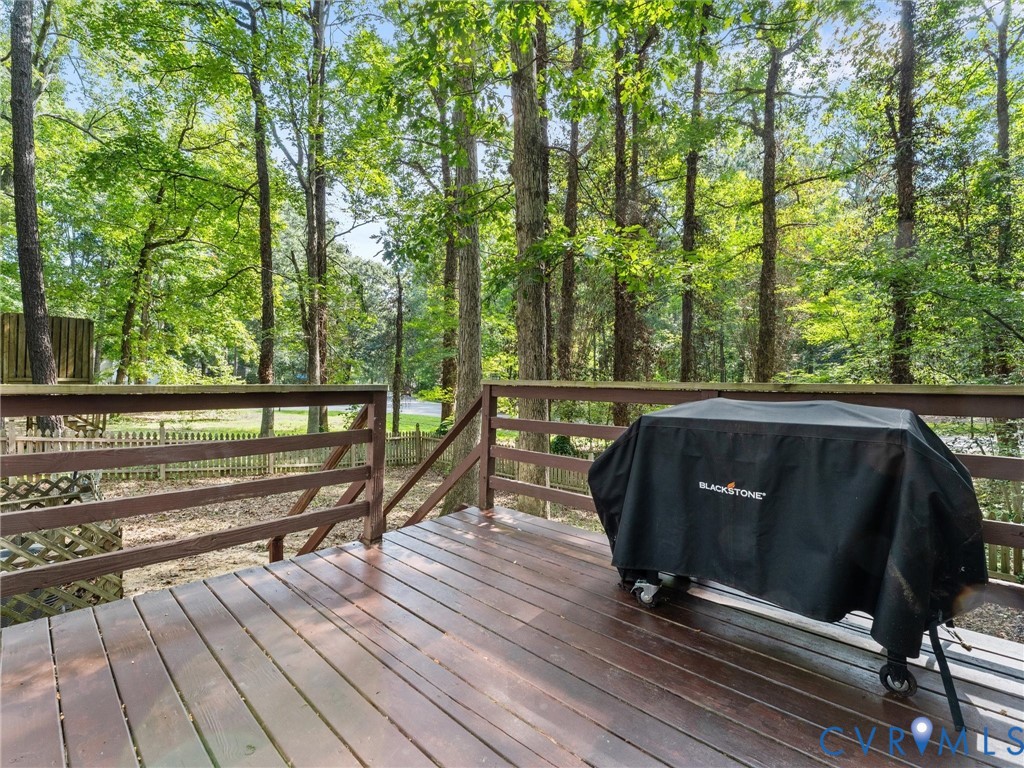 Elevated wood deck featuring a horizontal railing and expansive outdoor space shaded by mature trees