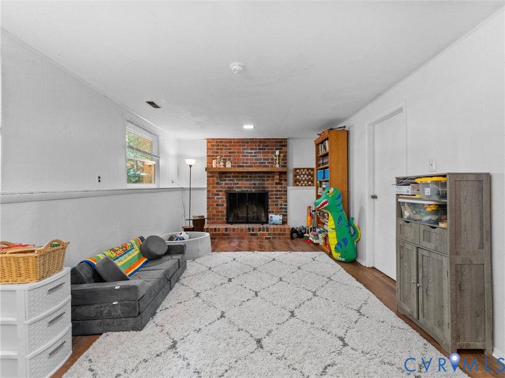 Brick fireplace featuring a wood mantel and metal firebox screen, accompanied by wood-finish flooring