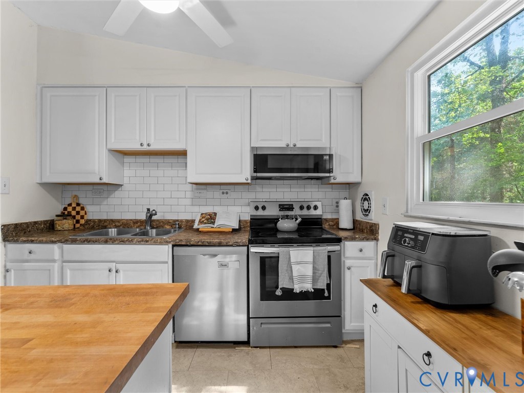 Kitchen featuring white cabinetry, subway tile backsplash, stainless steel appliances, butcher block countertops, and a double-basin sink