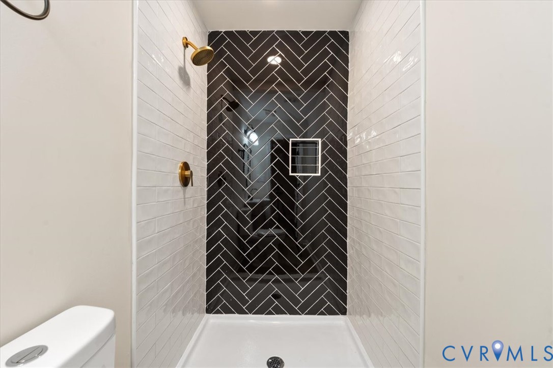 Shower enclosure featuring a black herringbone tile accent wall, white subway tile surround, brass-finish shower hardware, and a built-in recessed wall niche
