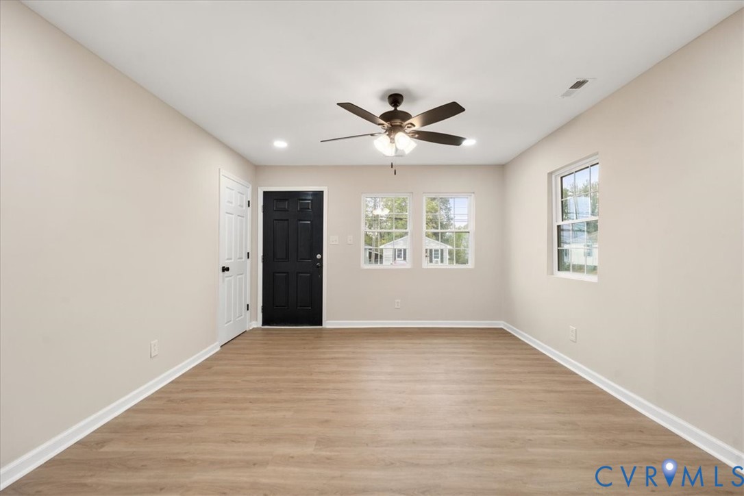 Neutral-toned interior featuring wood-finish flooring, recessed lighting, a ceiling fan with integrated lighting, dual-pane windows, and a contrasting black entry door Neutral-toned interior featuring wood-finish flooring, recessed lighting, a ceiling fan with integrated lighting, dual-pane windows, and a contrasting black entry door