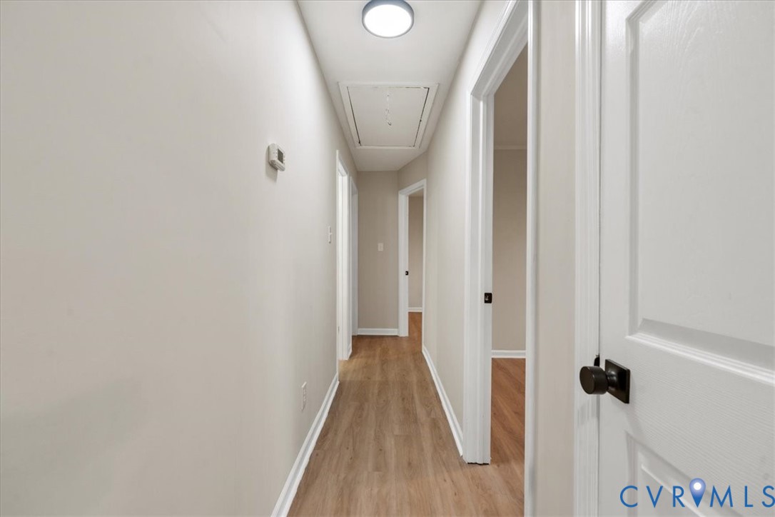 Interior hallway featuring wood-finish flooring, crisp neutral walls, white interior doors with matte black hardware, and a flush-mount circular ceiling light