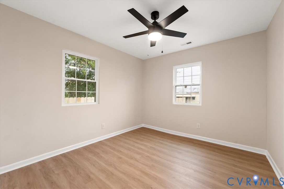 Interior room featuring wood-finish flooring, neutral wall paint, two dual-pane windows, and a matte black ceiling fan with integrated lighting