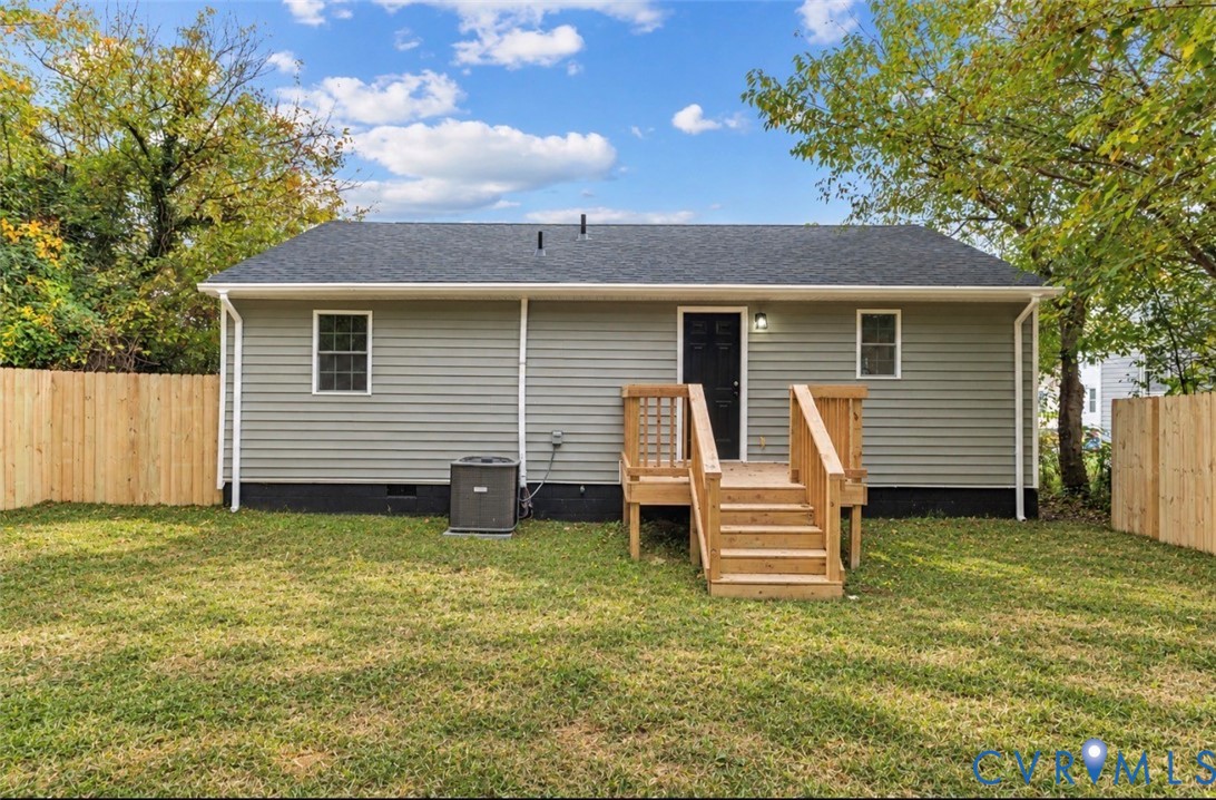 Rear exterior featuring gray vinyl siding, a wooden deck with stairs, a dark-toned door, and a perimeter wood privacy fence