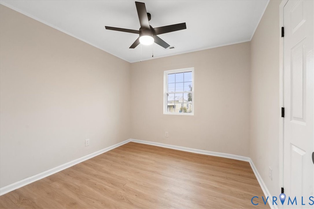 Neutral-toned interior featuring wood-finish flooring, a white single-pane window, and a ceiling fan with integrated lighting