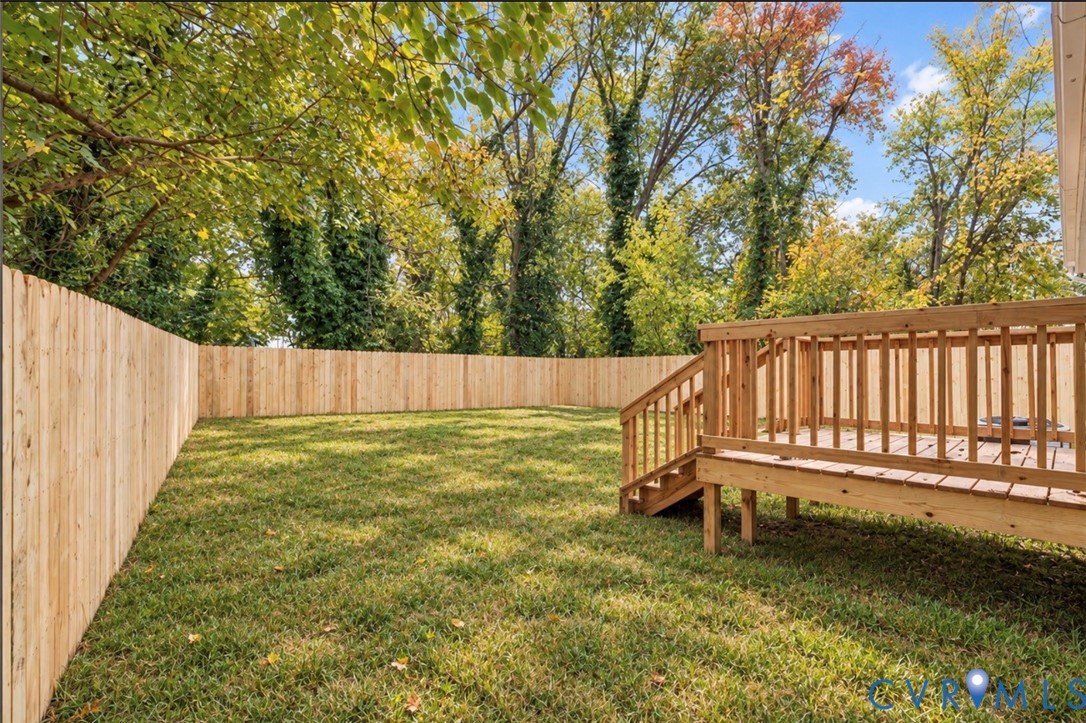 Backyard featuring a wood privacy fence, elevated wooden deck with stairs, and mature trees