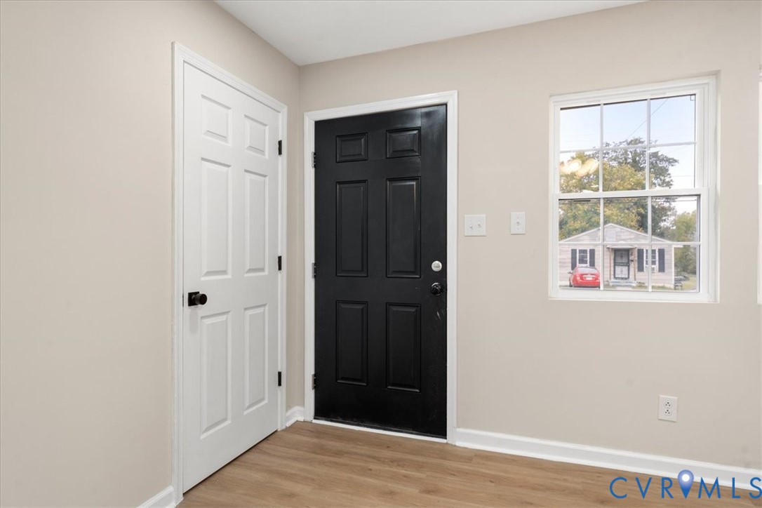 Entryway featuring wood-finish flooring, a six-panel exterior door in matte black, a matching six-panel interior door, and a single-hung window with a grid pattern Entryway featuring wood-finish flooring, a six-panel exterior door in matte black, a matching six-panel interior door, and a single-hung window with a grid pattern