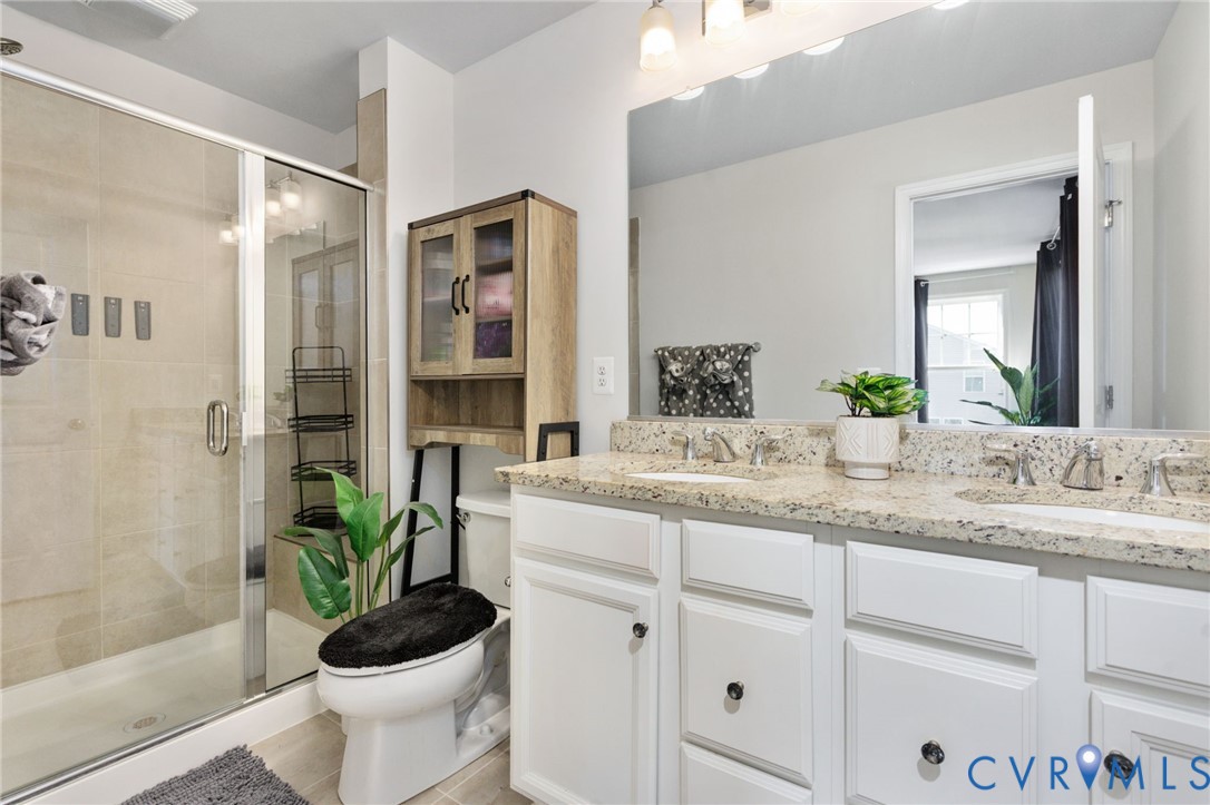 The private primary bath features a double-sink vanity, ample cabinet storage, and a glass-enclosed shower with tile surround.