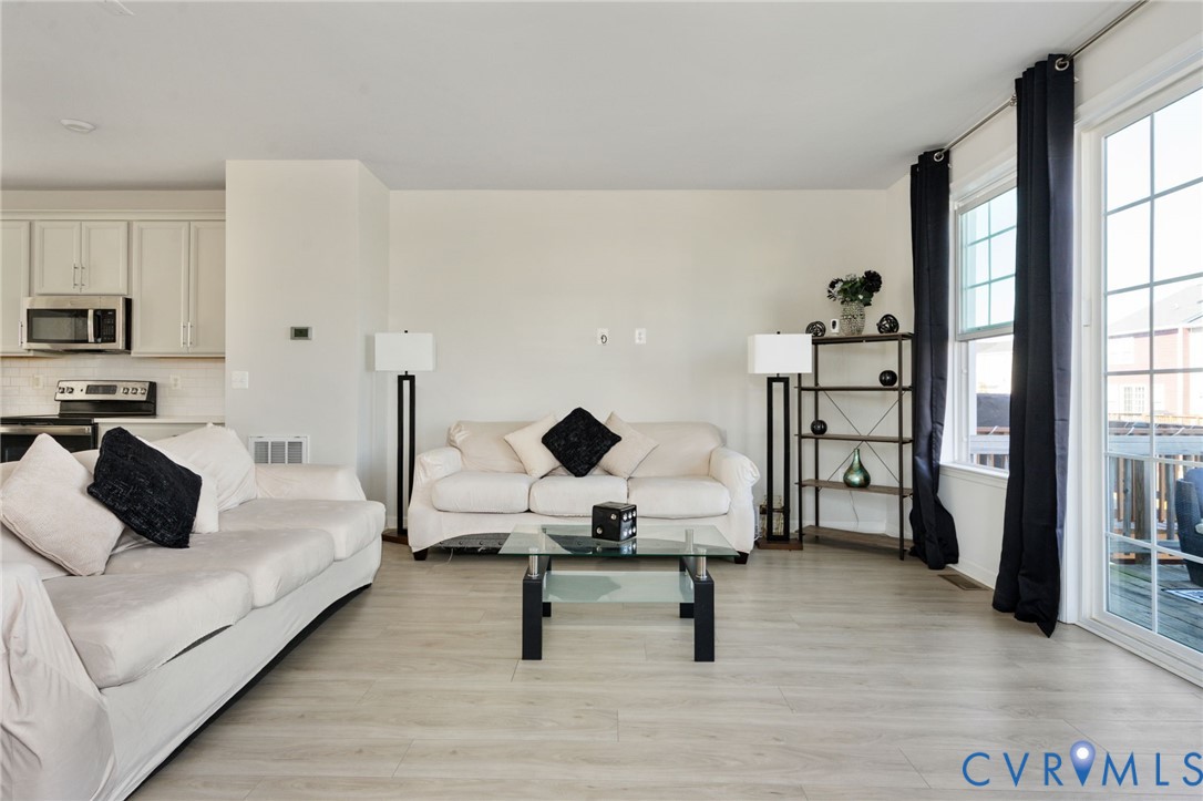 Open-concept living space featuring wood-finish flooring, white cabinetry, a built-in microwave, and large sliding glass doors