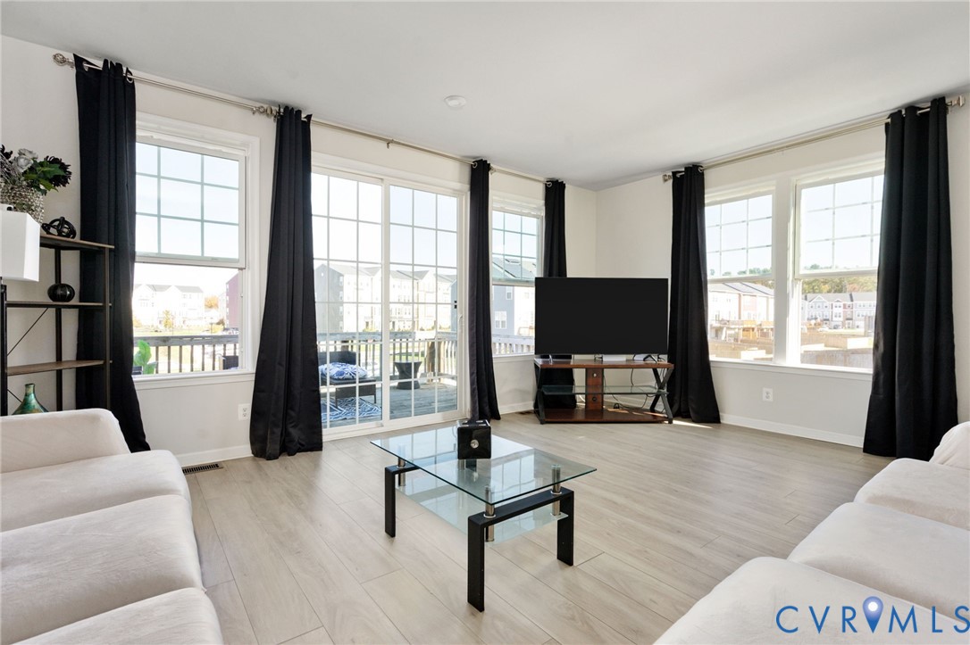 Open-concept area featuring light-toned wood-finish flooring, multi-pane windows, and sliding glass doors with access to an exterior deck