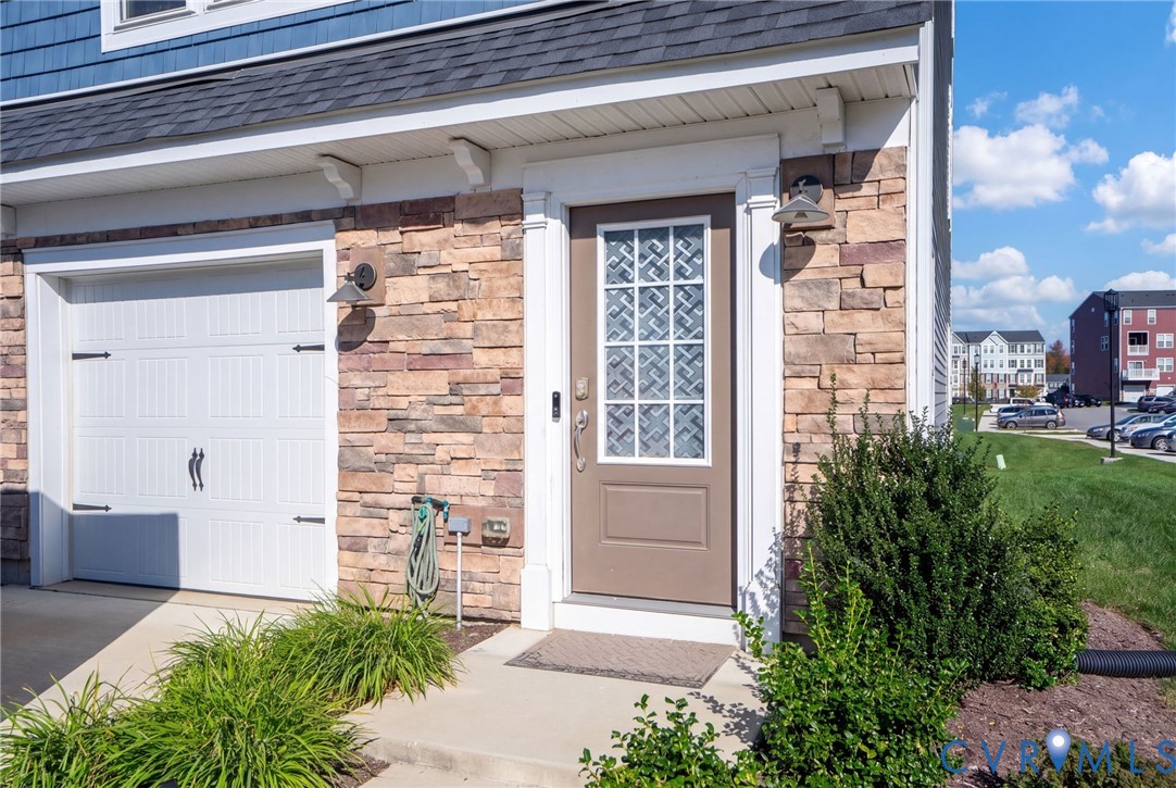 A glass-paneled front door, stone accents, and landscaped planting beds create a welcoming entrance beside the attached one-car garage. A glass-paneled front door, stone accents, and landscaped planting beds create a welcoming entrance beside the attached one-car garage.