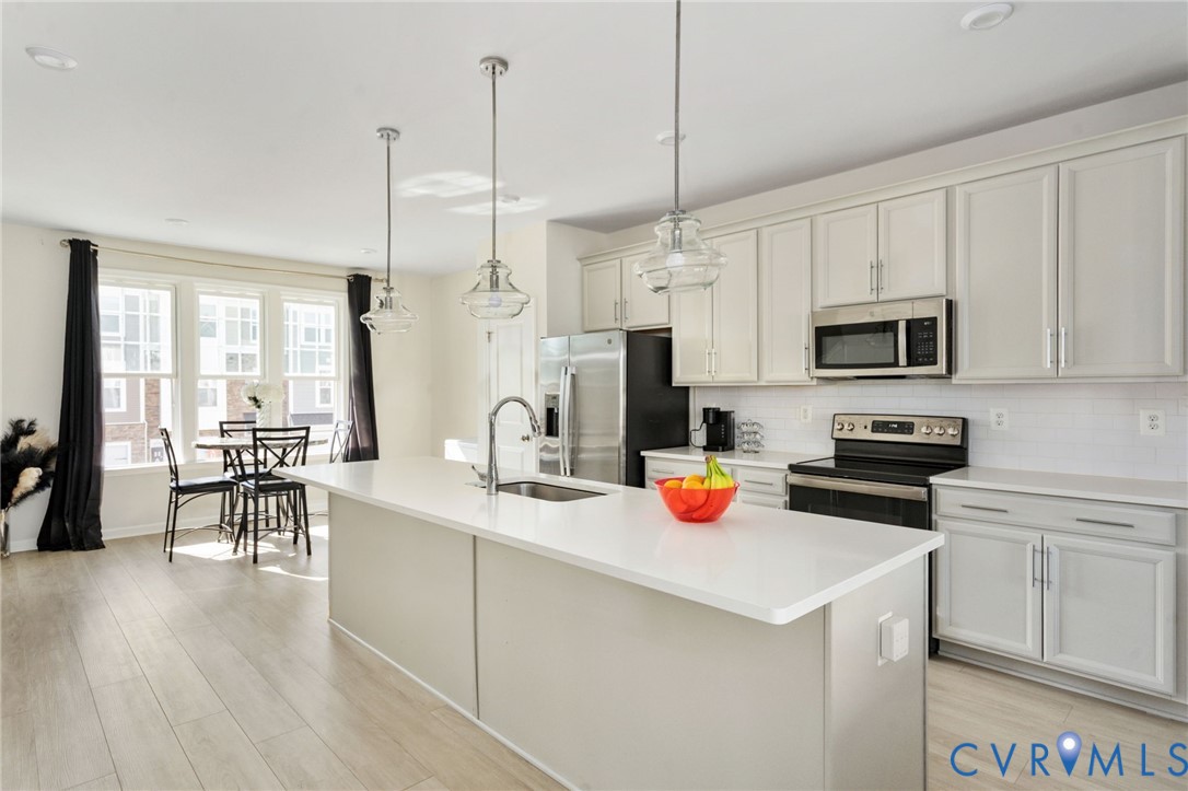This bright, open kitchen features white cabinetry, stainless steel appliances, a subway tile backsplash, and a spacious island with pendant lighting, all flowing into a sunny dining area. This bright, open kitchen features white cabinetry, stainless steel appliances, a subway tile backsplash, and a spacious island with pendant lighting, all flowing into a sunny dining area.