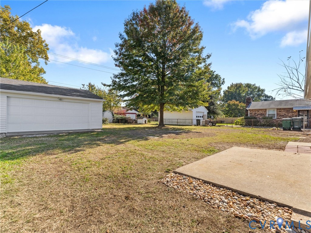 Rear exterior featuring a concrete patio, stone perimeter, detached garage, and mature trees within a fenced yard