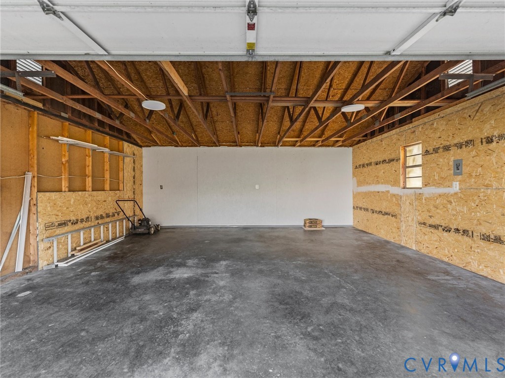 Attached garage featuring concrete flooring, exposed wood-truss ceiling, and oriented strand board wall paneling