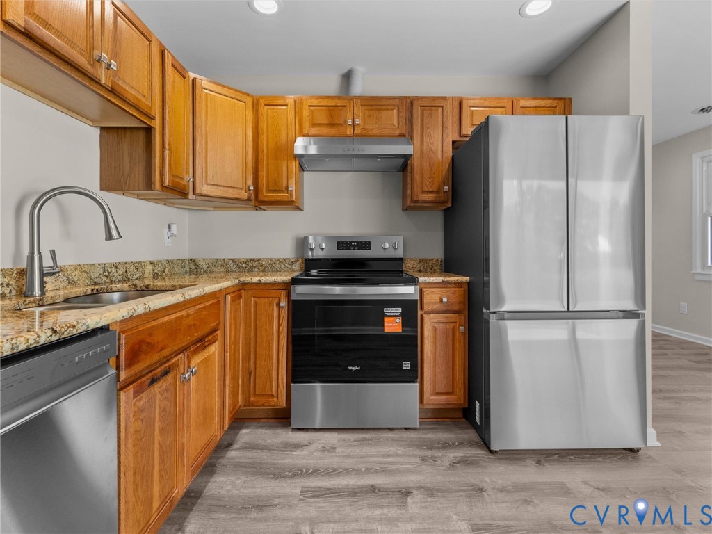 Kitchen featuring wood cabinetry, stone countertops, stainless steel appliances, a high-arc faucet, and wood-finish flooring