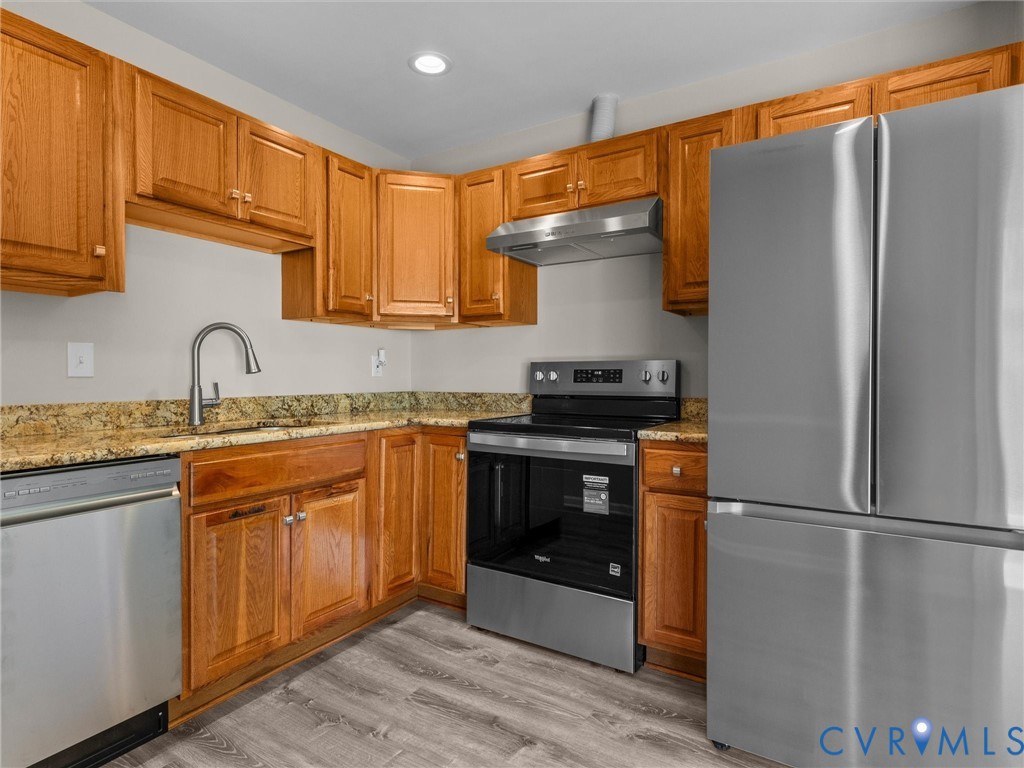 Kitchen featuring wood cabinetry, stone countertops, stainless steel appliances, a high-arc faucet, and wood-finish flooring