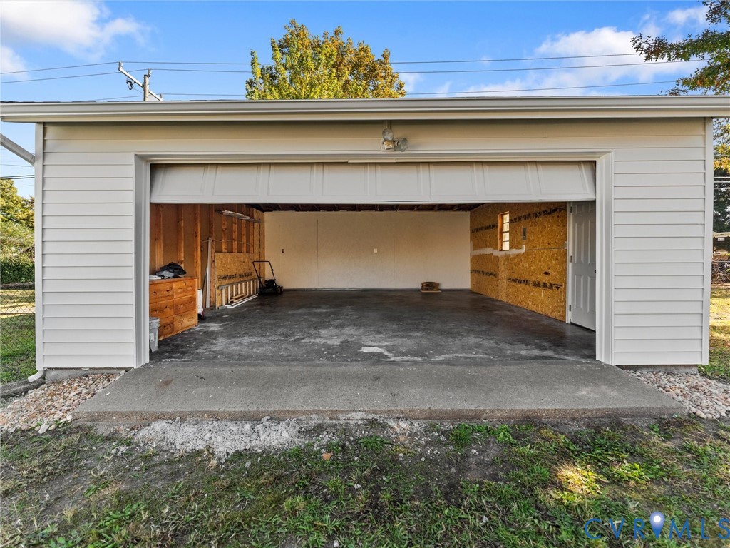 Detached garage featuring white horizontal siding, a concrete floor, a wide roll-up door, and a separate side entry door