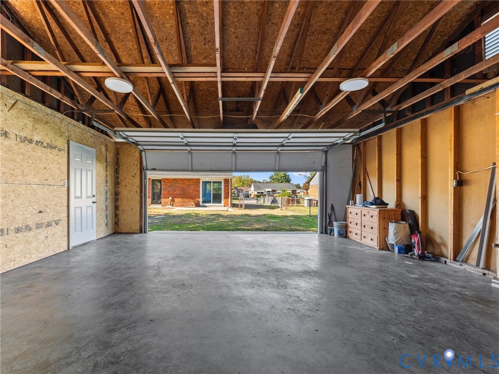 Detached garage featuring exposed wood framing, concrete flooring, overhead lighting, and a single pedestrian entry door