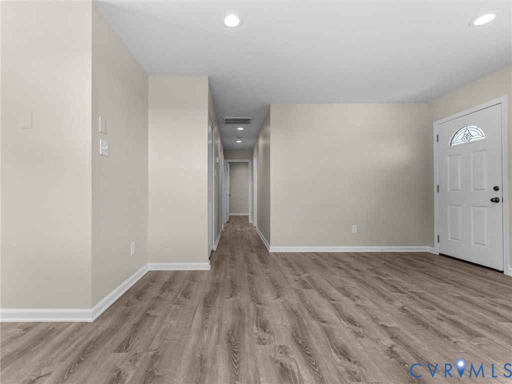 Interior space featuring wood-finish flooring, neutral wall paint, recessed lighting, and a six-panel exterior door with an arched decorative glass insert Interior space featuring wood-finish flooring, neutral wall paint, recessed lighting, and a six-panel exterior door with an arched decorative glass insert