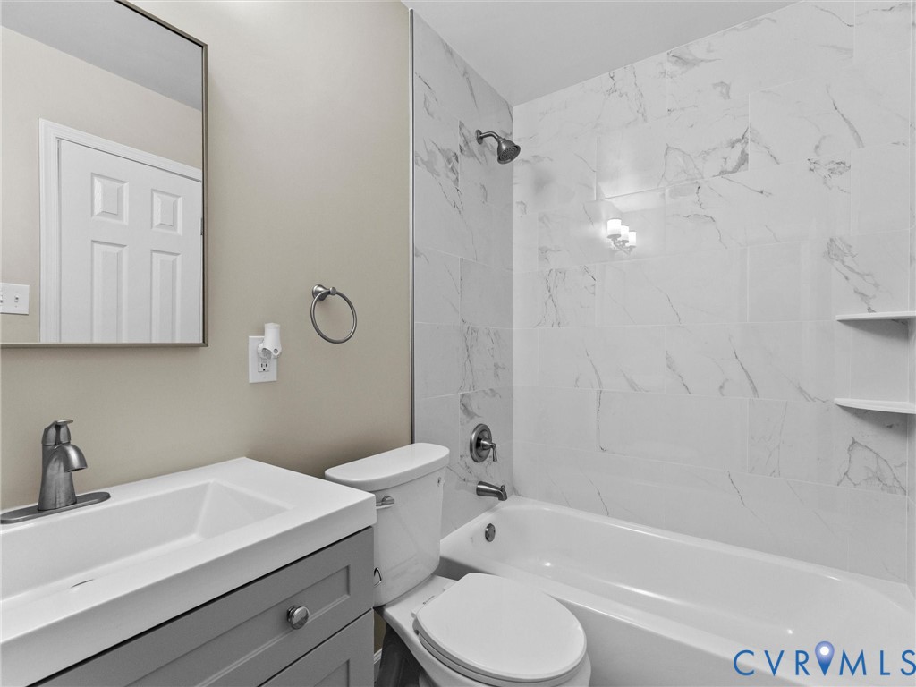 Bathroom featuring a gray vanity with a rectangular sink, wall-mounted mirror, tub-shower combination with light-veined tile surround, and integrated shelving