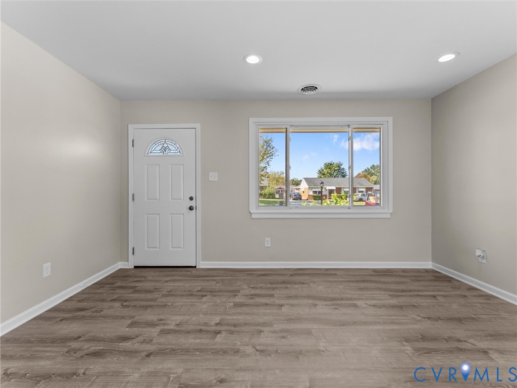 Interior space featuring wood-finish flooring, neutral wall paint, recessed lighting, and a six-panel exterior door with a semi-circular transom window Interior space featuring wood-finish flooring, neutral wall paint, recessed lighting, and a six-panel exterior door with a semi-circular transom window