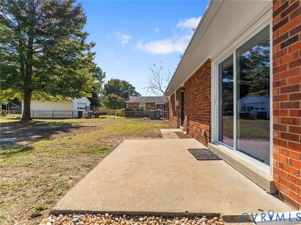 Red brick exterior featuring a concrete patio, sliding glass door, and expansive rear grounds with mature trees