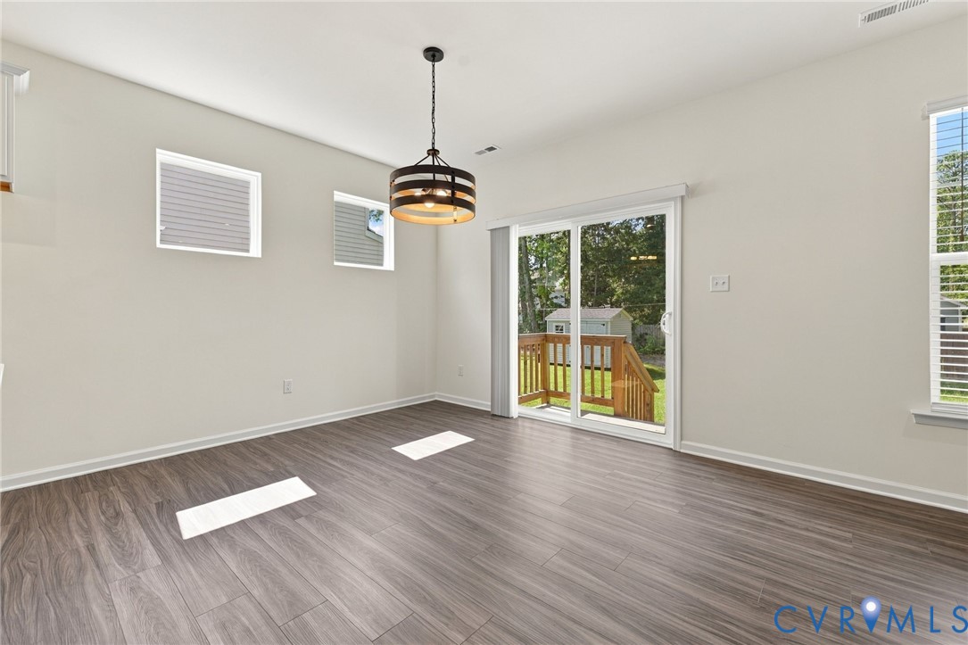 Wood-finish flooring, industrial-style drum pendant light, multi-pane windows, and sliding glass door with exterior access