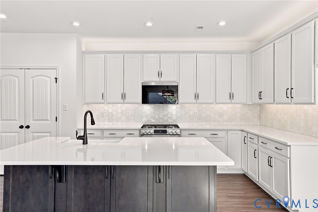 Kitchen featuring white shaker cabinetry, an expansive center island with a dark-toned base, stone-style countertops, a honeycomb-patterned tile backsplash, and a matte black gooseneck faucet