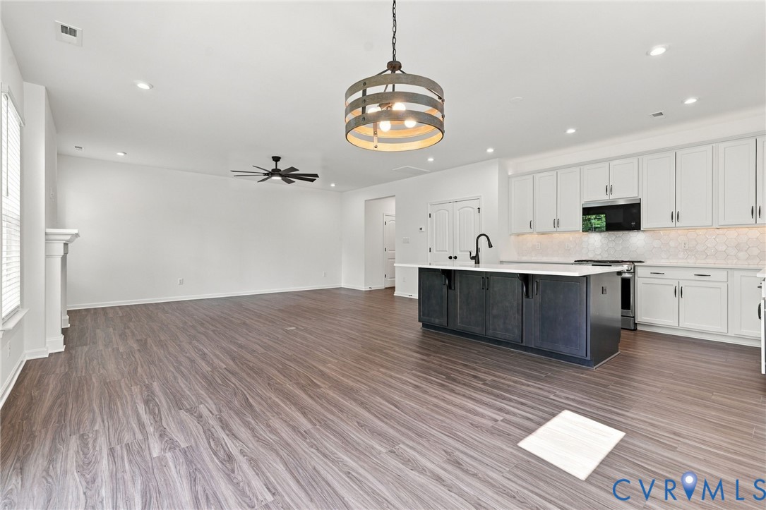 Kitchen featuring a dark-toned central island with a white countertop, shaker-style white cabinetry, wood-finish flooring, a metal drum pendant light, and recessed lighting