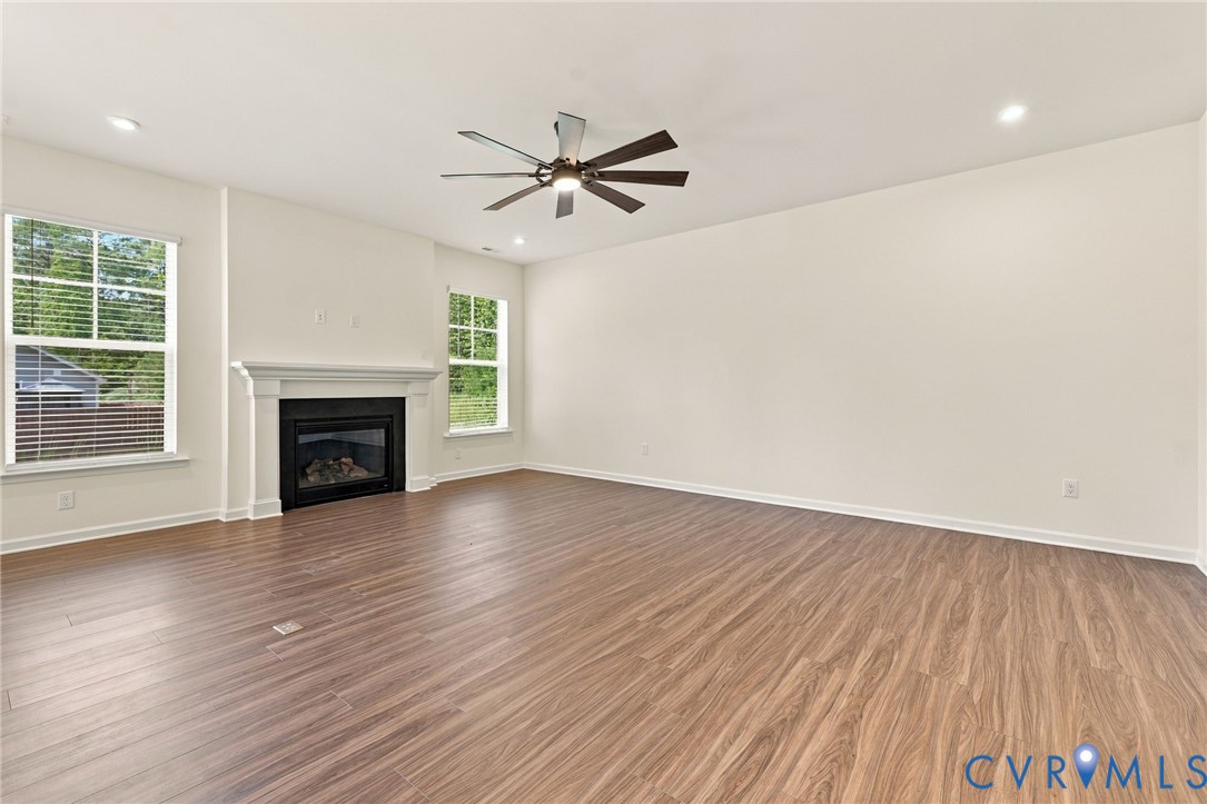 Wood-finish flooring, fireplace with a decorative mantel, ceiling fan, and large windows with horizontal blinds