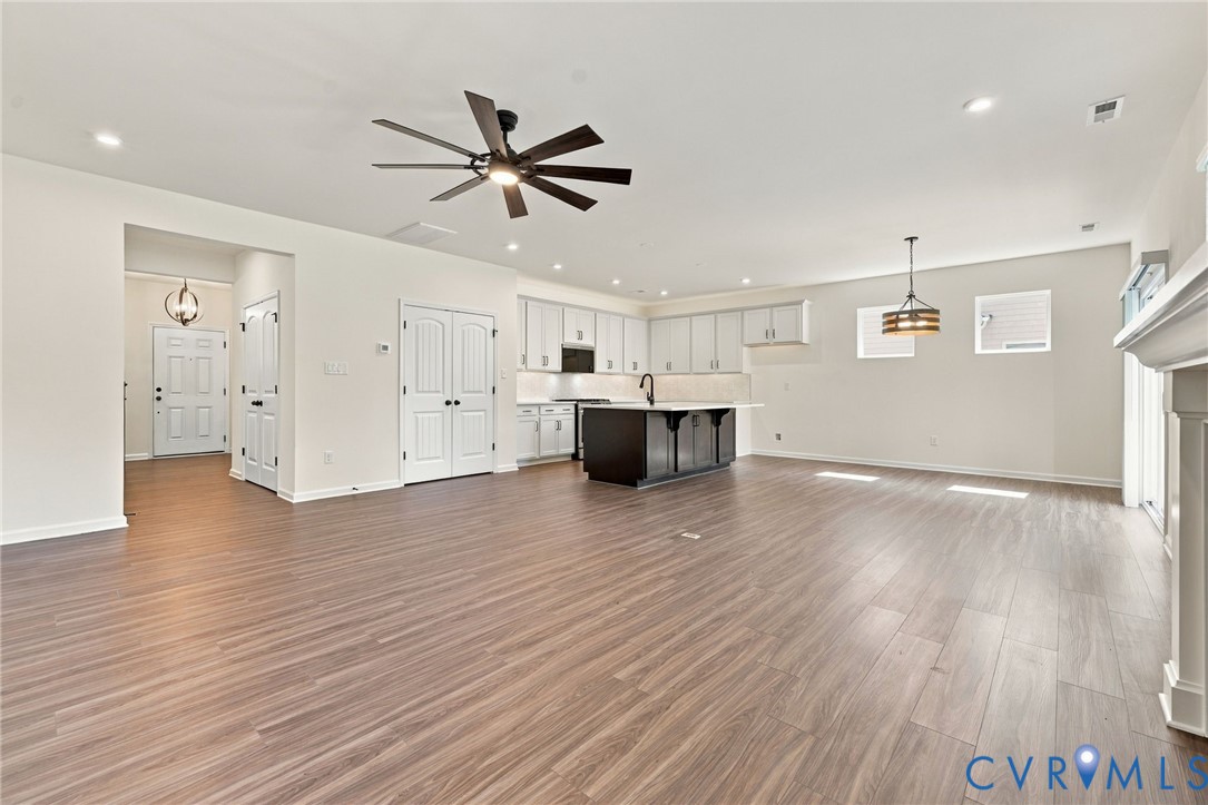 Open-concept kitchen and living area featuring wood-finish flooring, a center kitchen island with dark cabinetry, white perimeter cabinetry, recessed lighting, and a multi-blade ceiling fan
