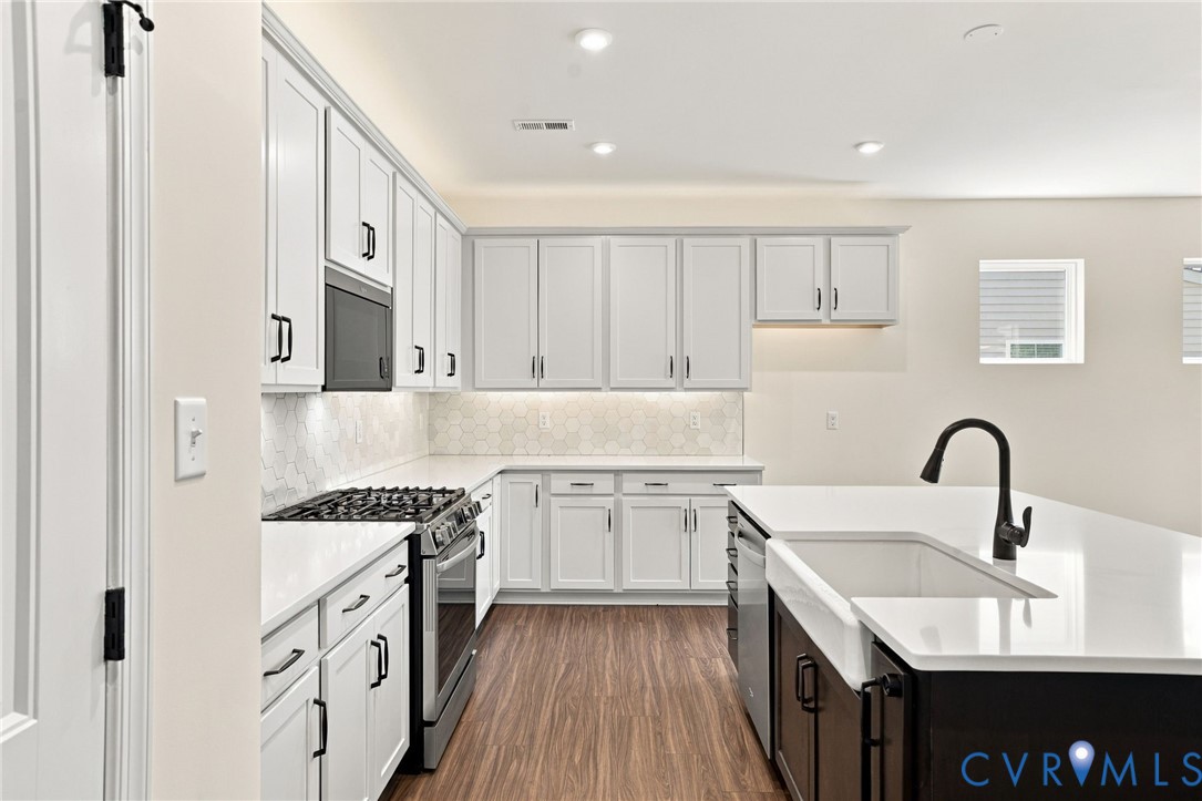 Kitchen featuring white shaker-style cabinetry, a contrasting dark kitchen island, solid-surface countertops, a farmhouse-style sink with a matte black faucet, and patterned backsplash tile
