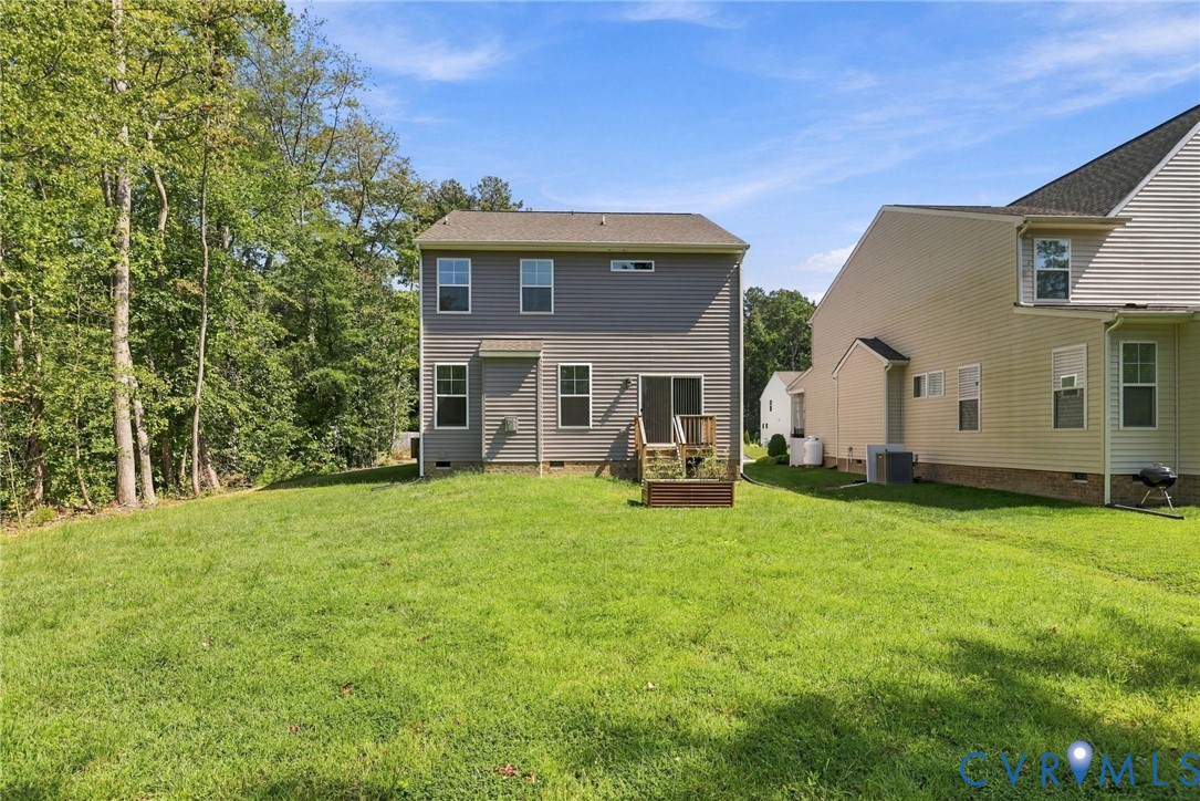 Rear exterior featuring horizontal vinyl siding, multi-level windows, a sliding glass door, and an attached wood deck overlooking a grassy lawn with mature tree coverage