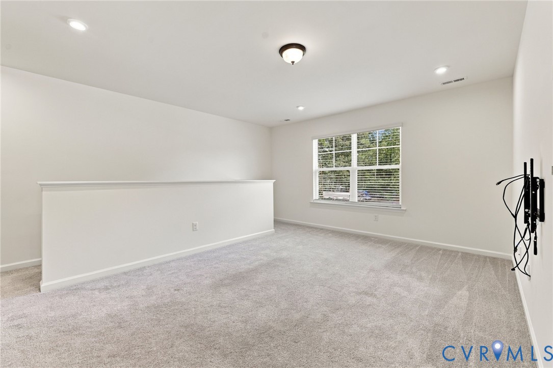 Neutral-toned wall-to-wall carpeting, recessed ceiling lighting, central flush-mount fixture, and large multi-pane window