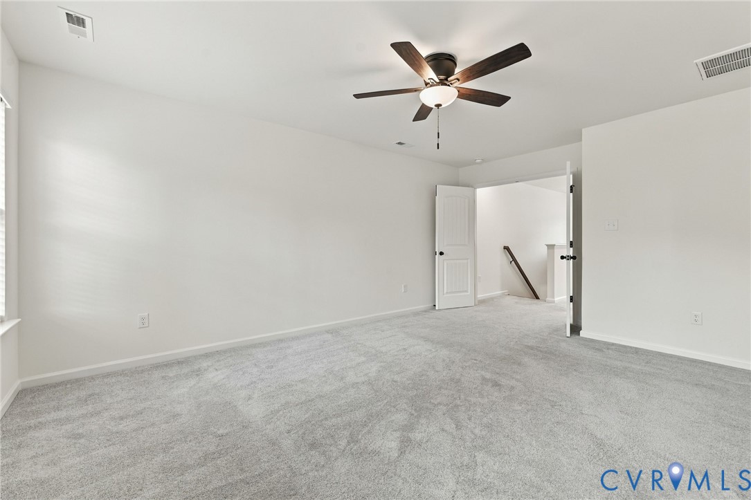 Neutral-toned wall-to-wall carpeting, ceiling fan with integrated lighting, and white six-panel interior door