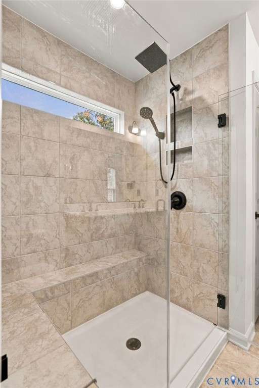 Walk-in shower featuring floor-to-ceiling tile, frameless glass enclosure, built-in bench seating, integrated wall niche, and rainfall showerhead with matte black finish hardware