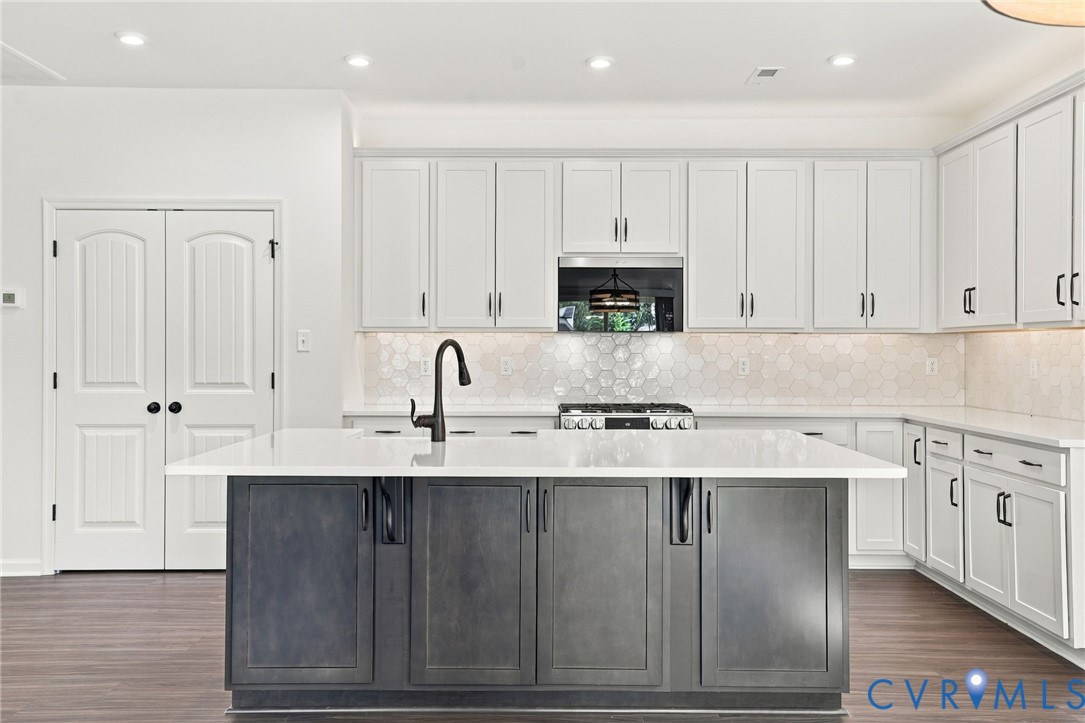 Kitchen featuring a center island with a stone countertop and dark-finish cabinetry, white wall-mounted cabinetry, hexagonal tile backsplash, wood-finish flooring, and a matte black gooseneck faucet