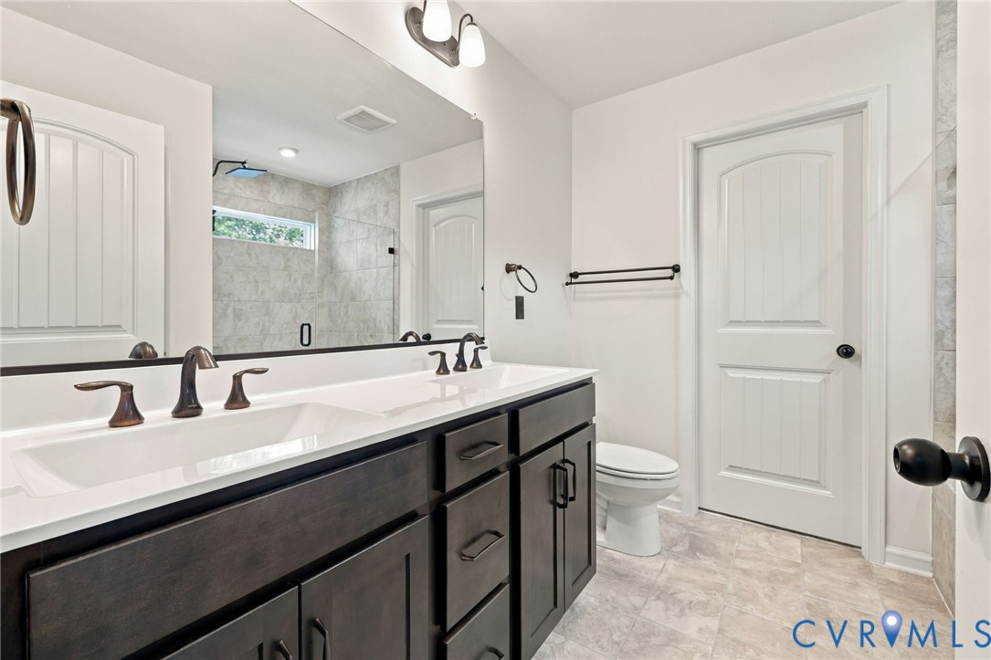 Dual-sink vanity with dark cabinetry and composite countertop, large wall-mounted mirror, matte black fixtures, and tiled walk-in shower