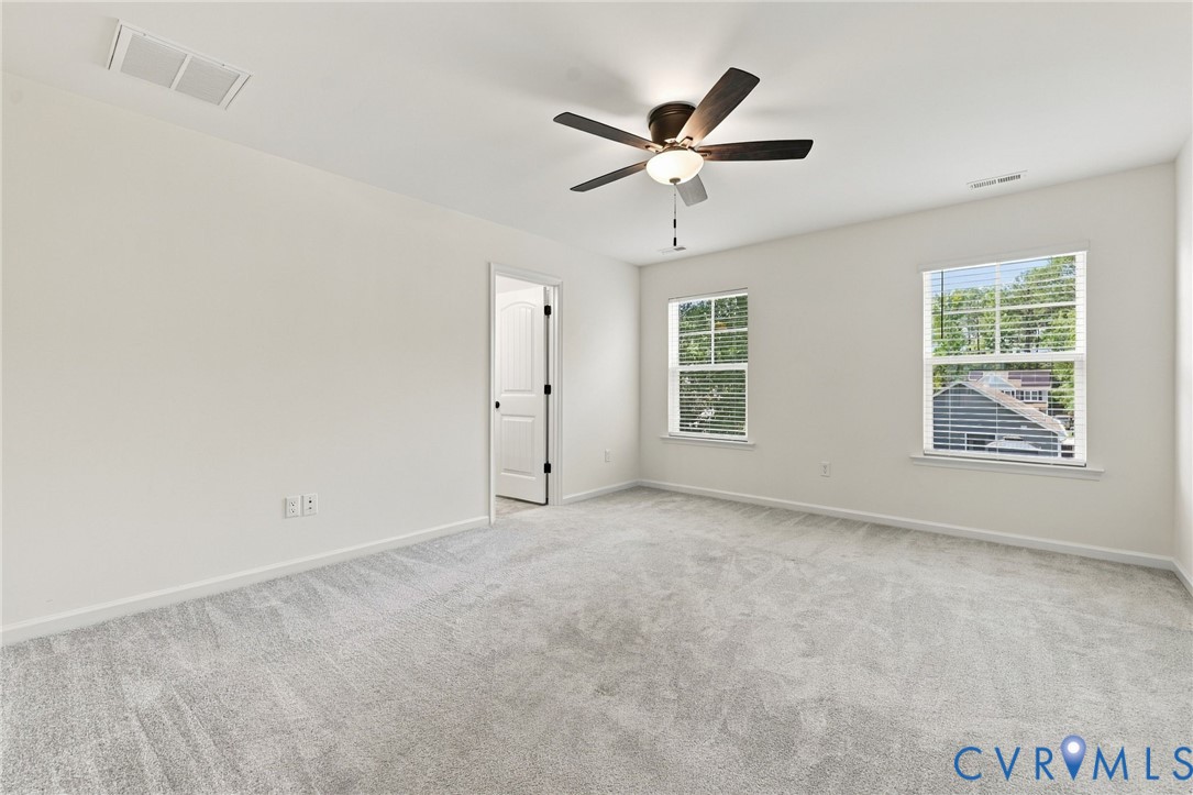 Neutral-toned carpeting, dual windows, ceiling fan with integrated lighting, and interior door with matte black hardware