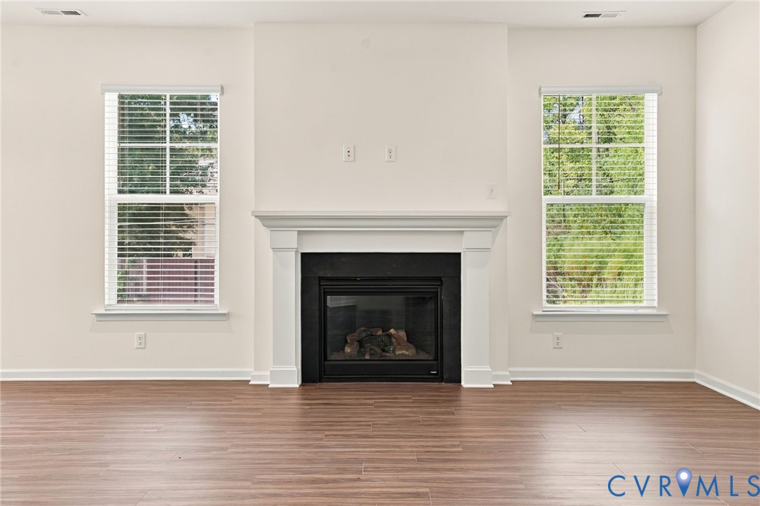 Fireplace with a black surround and white mantel, flanked by dual windows with blinds and wood-finish flooring