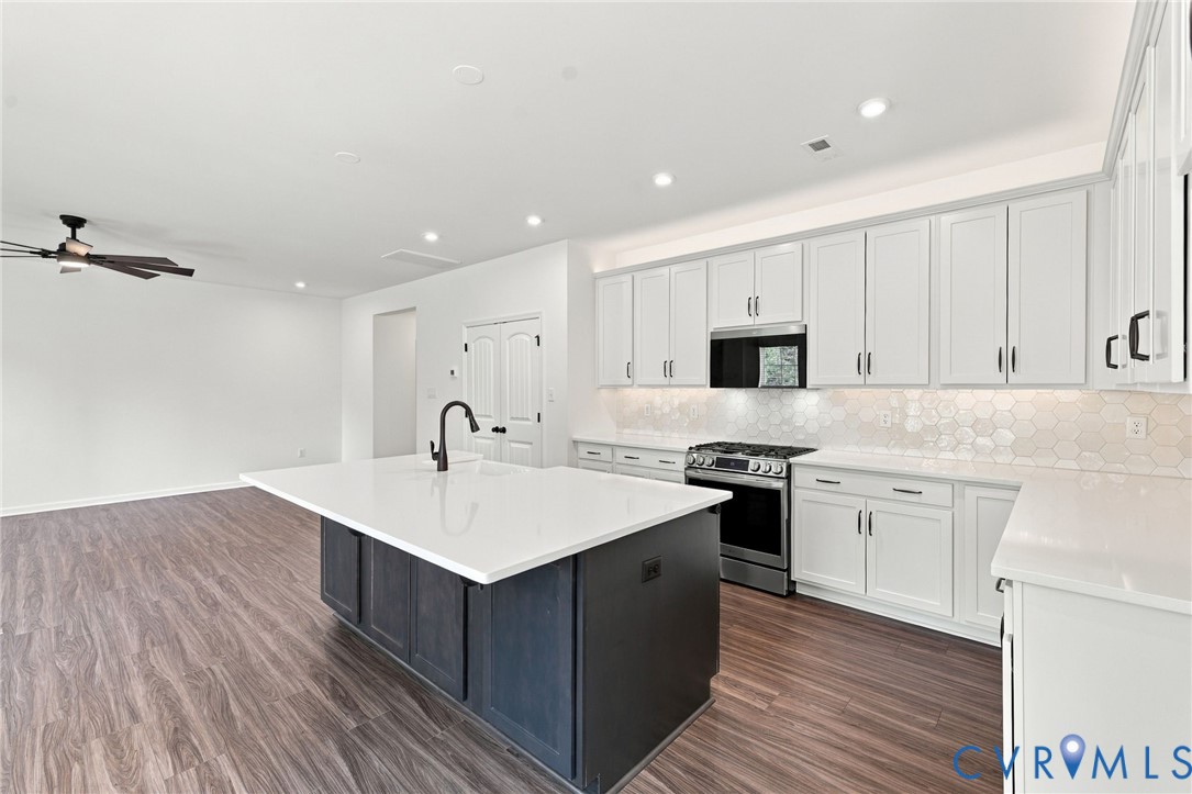 Kitchen featuring white cabinetry, a contrasting dark island, stone-finish countertops, geometric tile backsplash, and wood-finish flooring